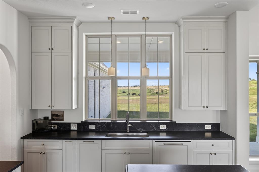 11032 Gregory Road Sanger, TX 76266 - Photo 20 of 40 White shaker-style cabinetry with crown molding, dark stone countertops with backsplash, stainless steel sink with a gooseneck faucet, and two pendant lights