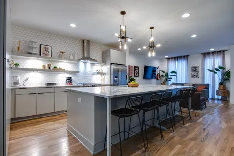 a kitchen with stainless steel appliances granite countertop a refrigerator a sink dishwasher a dining table and chairs with wooden floor