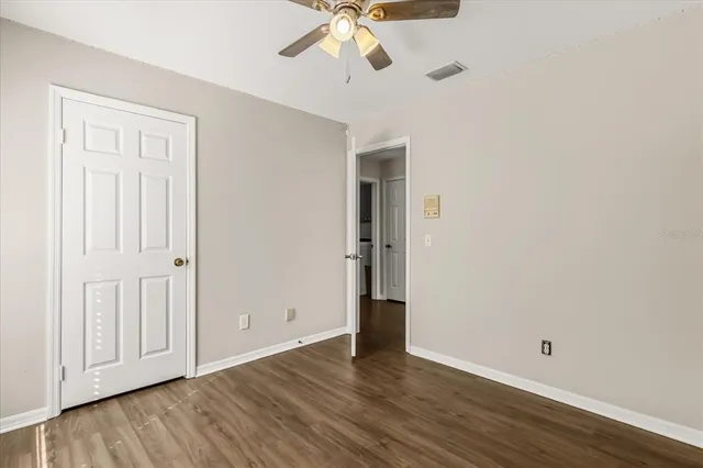 an empty room with wooden floor chandelier fan and windows