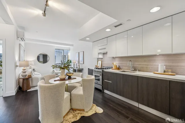 a living room with stainless steel appliances kitchen island granite countertop a refrigerator a sink dishwasher and white cabinets with wooden floor