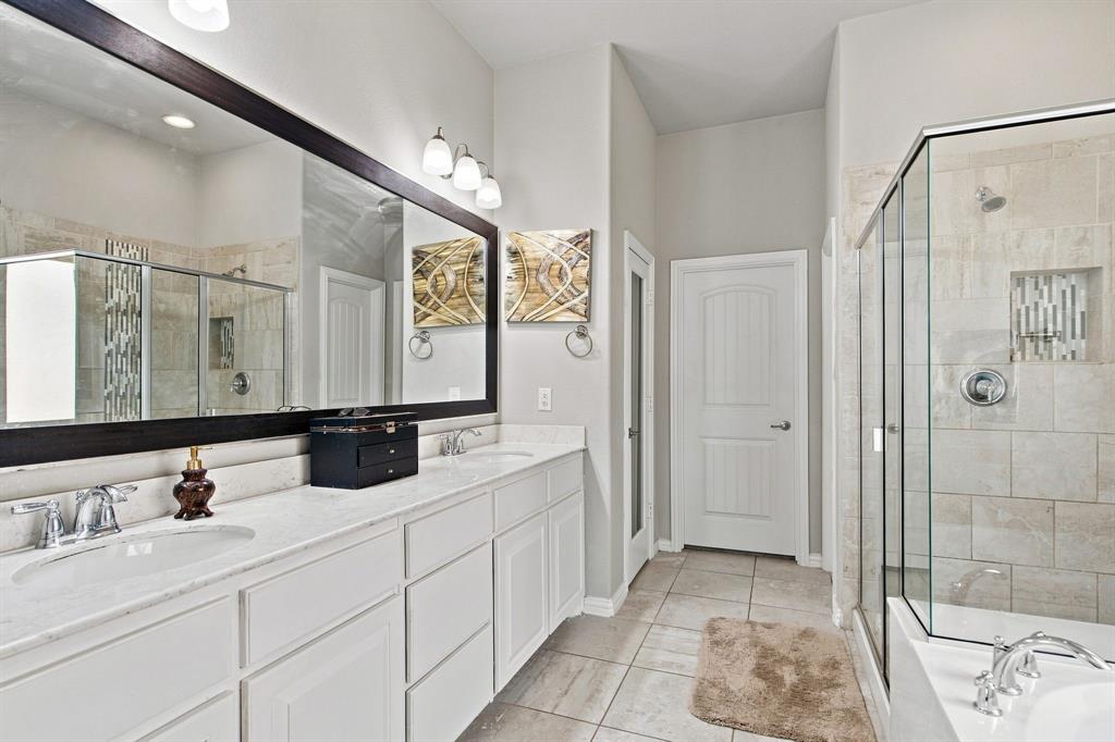 3908 Ranchman Boulevard Denton, TX 76210 - Photo 14 of 29 Dual vanity with white cabinetry and integrated sinks, extensive countertop space, large framed mirror, and a glass-enclosed shower with tiled surround