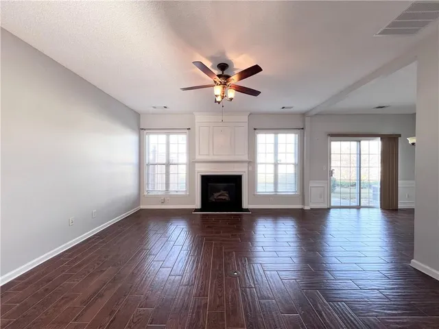 an empty room with wooden floor a ceiling fan a fireplace and windows