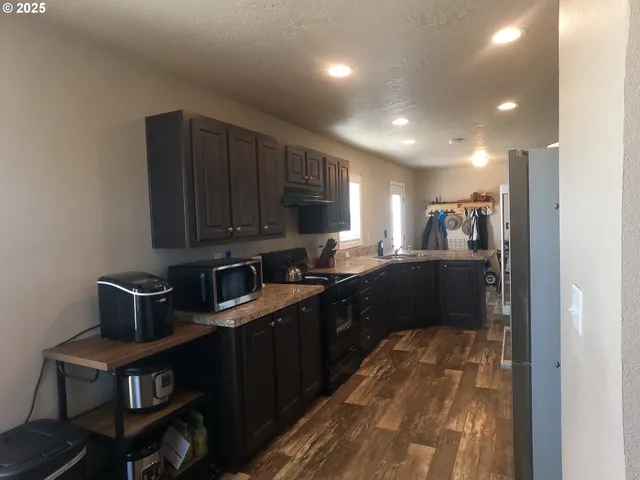 a kitchen with stainless steel appliances granite countertop a sink a stove a refrigerator cabinets and a dining table