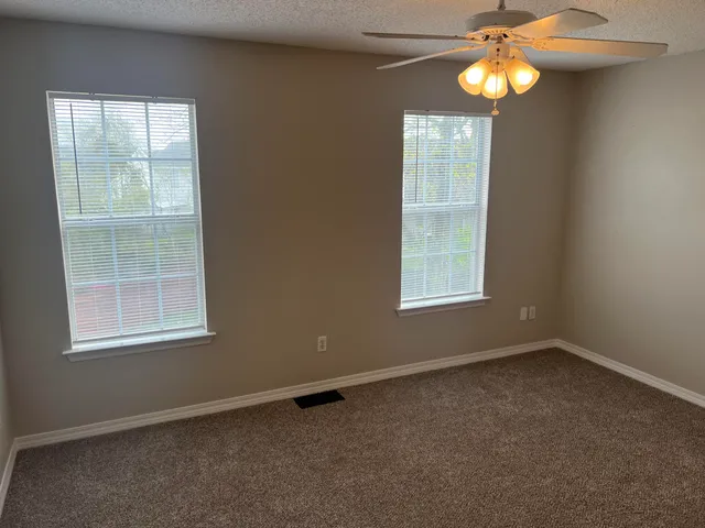 an empty room with windows and chandelier fan