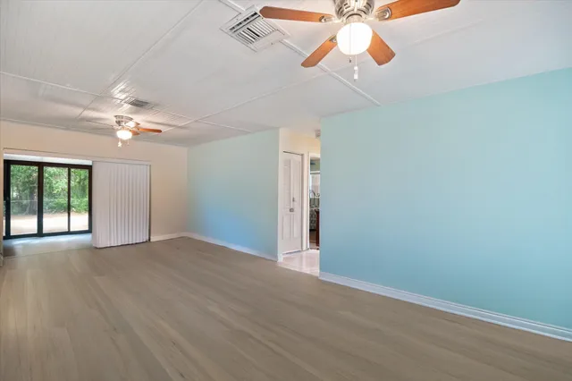 an empty room with chandelier fan and windows