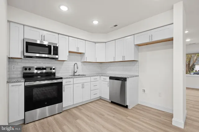 a kitchen with granite countertop white cabinets stainless steel appliances and a wooden floor