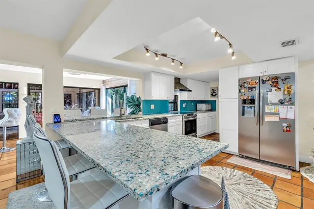 a kitchen with stainless steel appliances granite countertop a refrigerator a stove and white cabinets with wooden floor