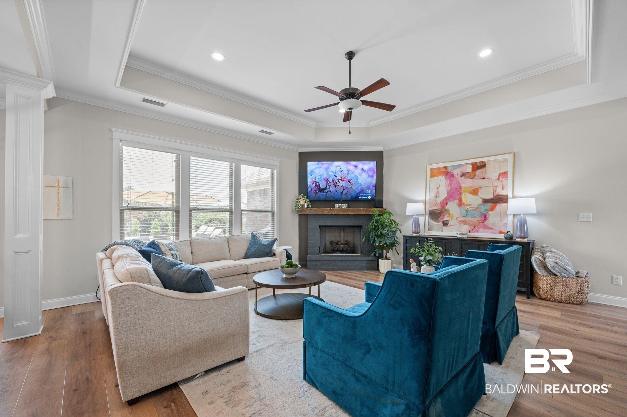 409 Fortune Drive Fairhope, AL 36532 - Photo 6 of 42 Spacious living area featuring high tray ceilings, wood-finish flooring, a corner fireplace with a dark surround, and large windows providing abundant light
