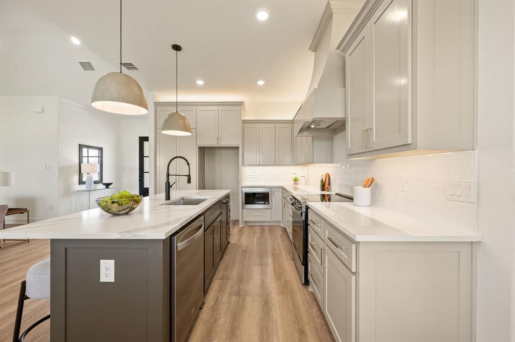 2705 Gospel Road Tolar, TX 76476 - Photo 14 of 36 Modern kitchen featuring a large island with sink, stainless steel appliances, light gray cabinetry, white countertops, and luxury vinyl flooring