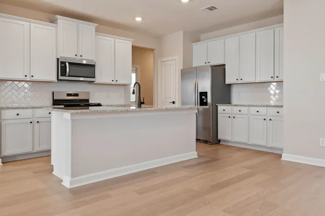 a view of kitchen with stainless steel appliances granite countertop a stove a sink a refrigerator and white cabinets with wooden floor