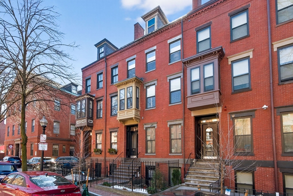 a front view of a building with lot of cars and trees