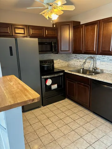 a kitchen with stainless steel appliances kitchen island granite countertop a refrigerator a sink and wooden cabinets