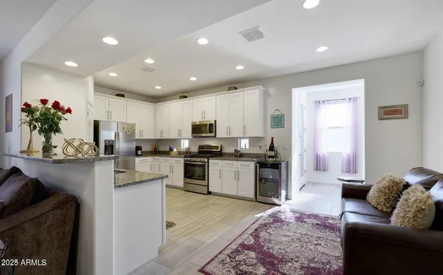a large white kitchen with stainless steel appliances granite countertop a stove a sink a refrigerator and a couch