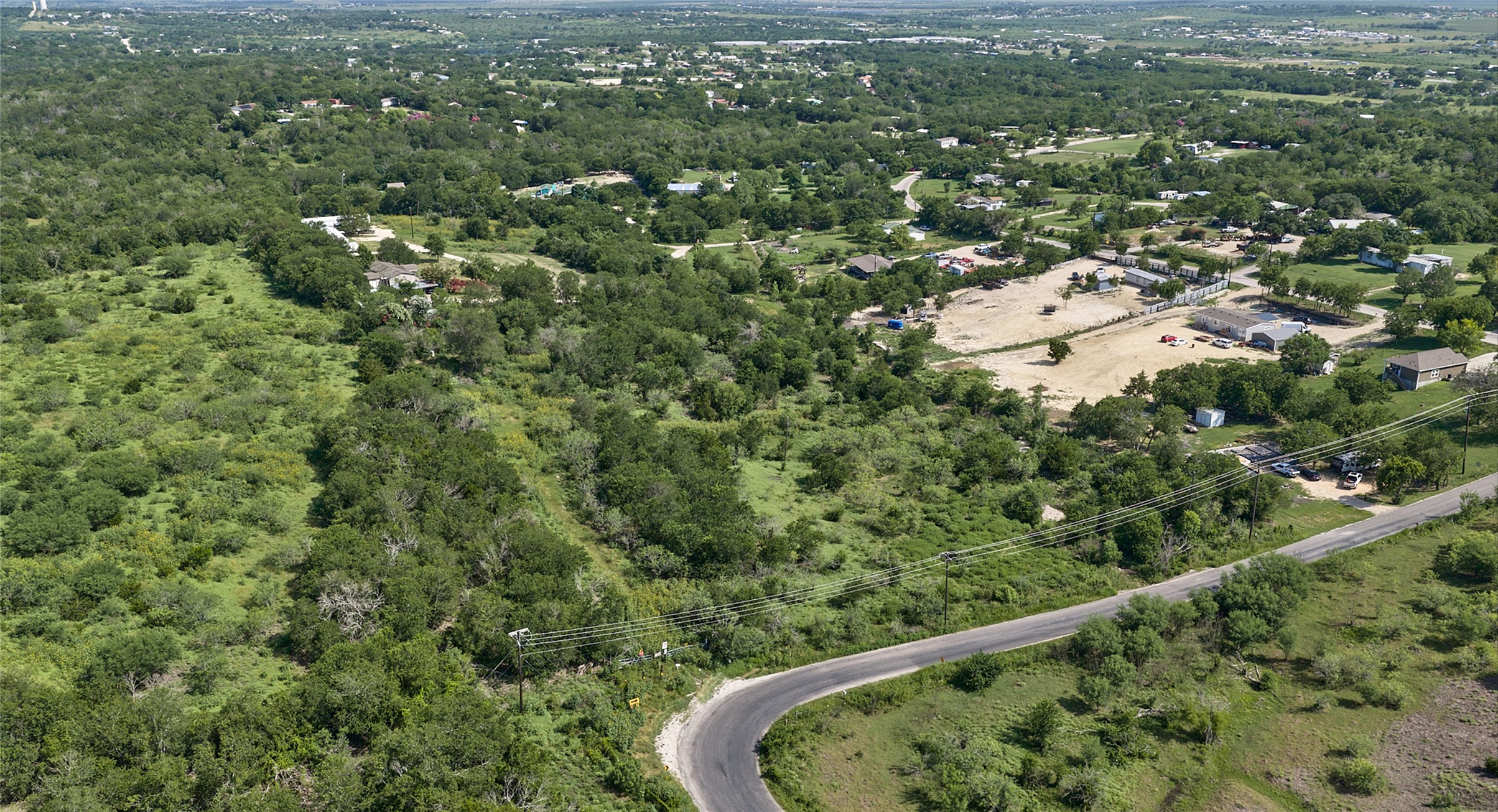 1400 Williamson Road Kyle, TX 78640 - Photo 4 of 13 An aerial perspective reveals the vast green landscape with a winding road and distant structures.