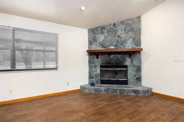 a view of an empty room with wooden floor fire place and a window