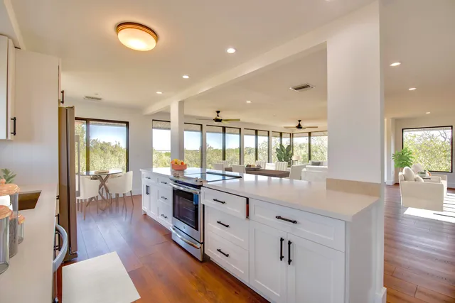 a kitchen with stainless steel appliances granite countertop a refrigerator a sink dishwasher a stove and a dining table with wooden floor