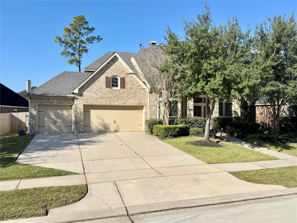 13626 Breakwater Path Loop Houston, TX 77044 - Photo 2 of 29 This home features a brick exterior with a three-car garage. The front yard is landscaped with mature trees and shrubs, offering a welcoming curb appeal.