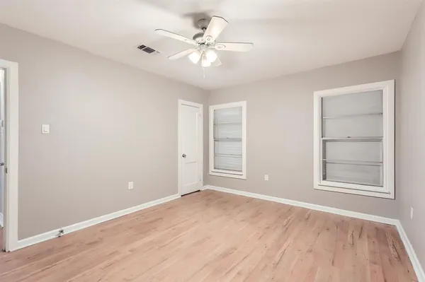 an empty room with wooden floor chandelier fan and windows