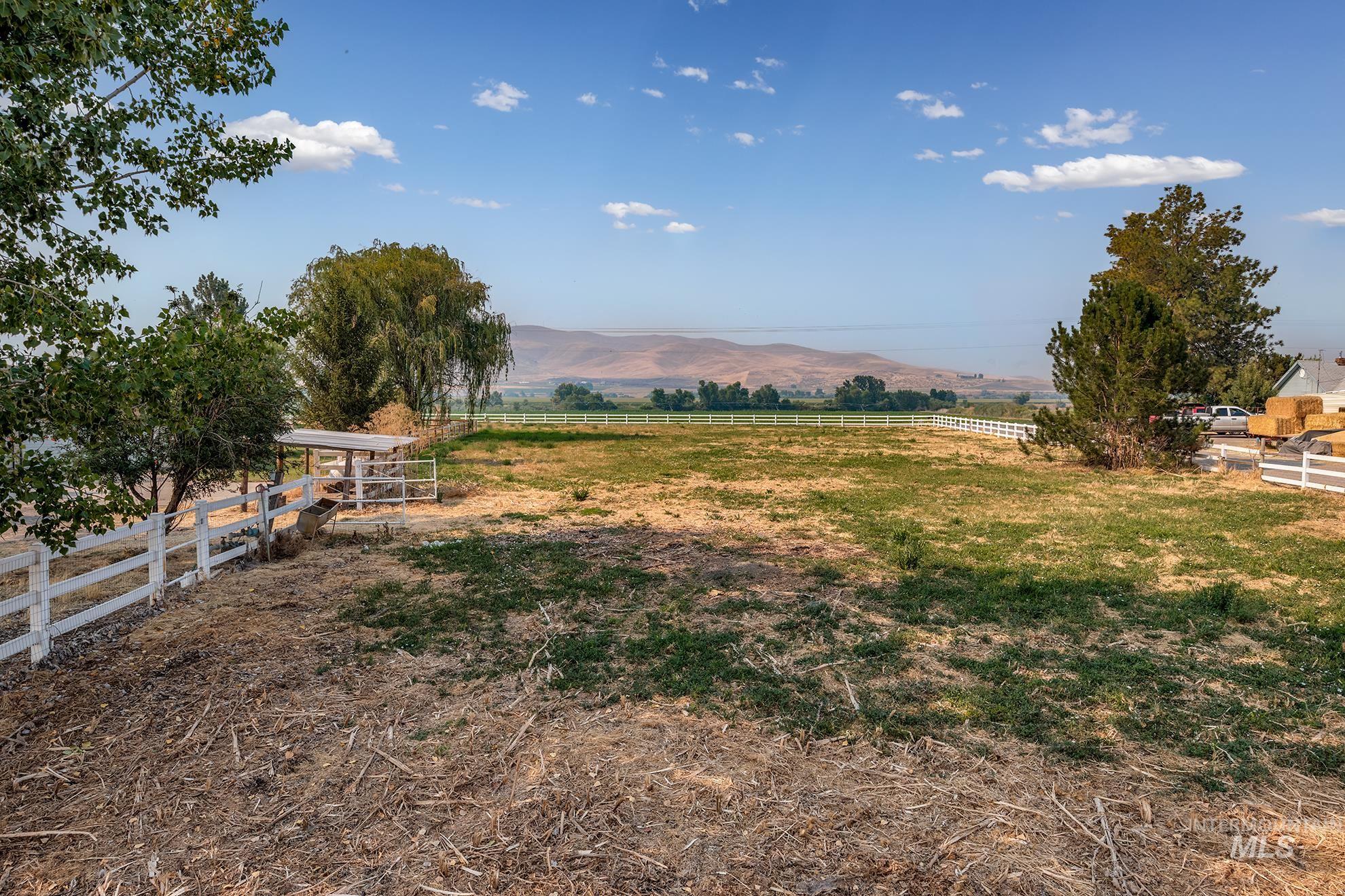 1741 Cove Road Weiser, ID 83672 - Photo 40 of 46 Expansive property featuring a white rail fence, mature trees, a covered outdoor structure, and distant mountain scenery