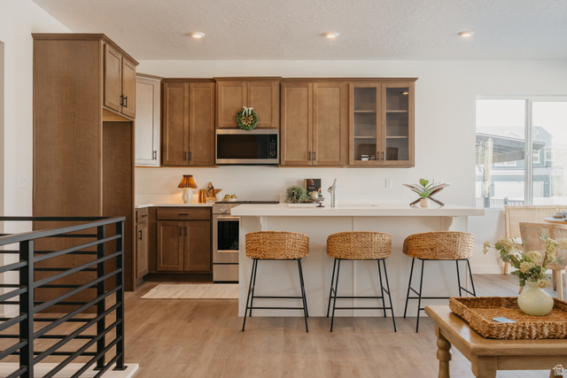 4595 North Fallow Way, Unit 511 Eagle Mountain, UT 84005 - Photo 21 of 32 Kitchen featuring wood finish cabinetry, a breakfast bar, stainless steel appliances, glass insert cabinets, and light wood-style floors