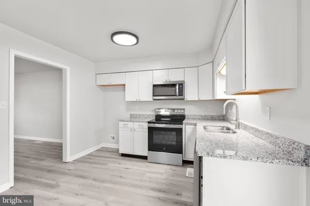 a kitchen with granite countertop a sink dishwasher stove and microwave with wooden floor