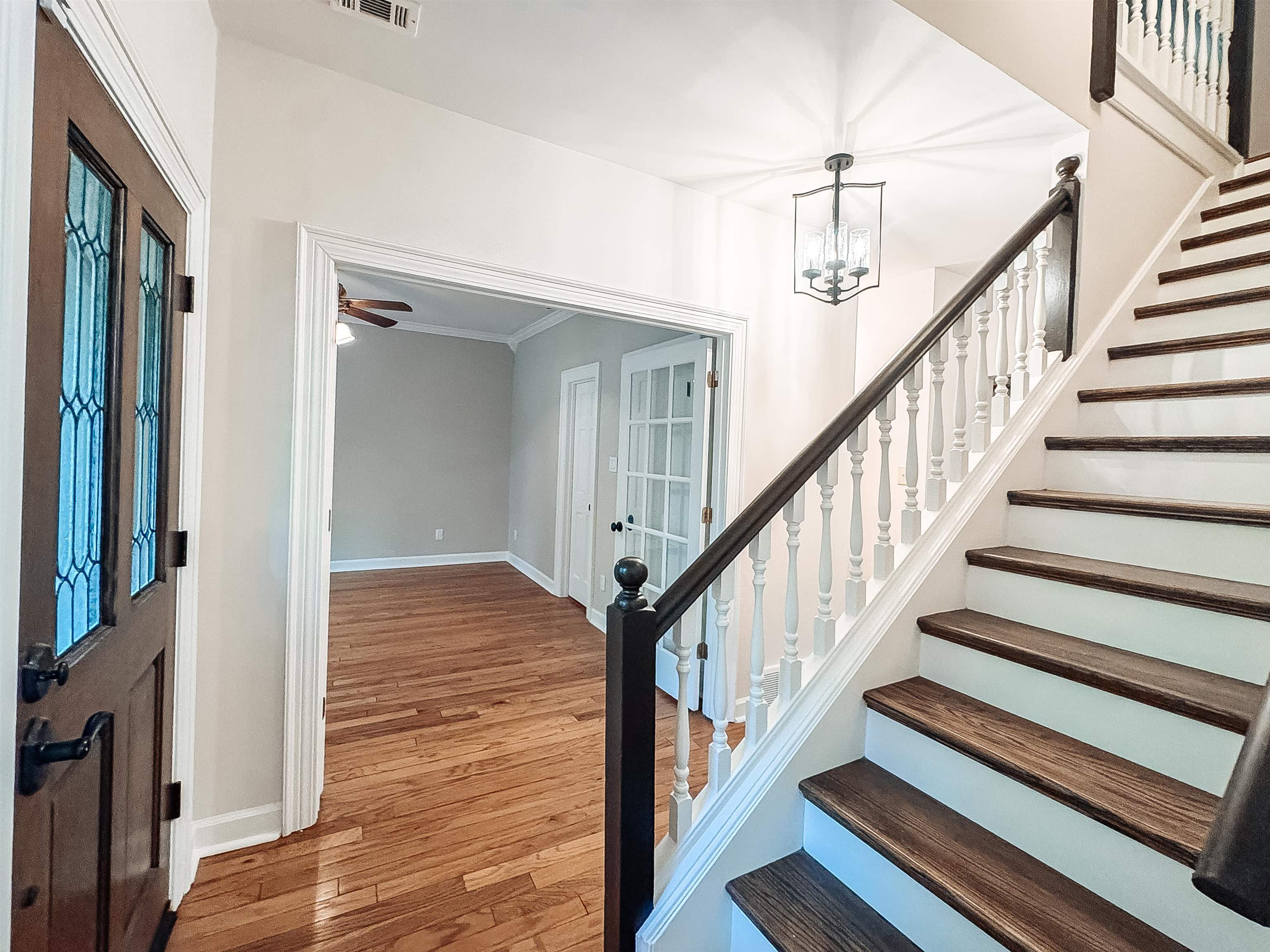 832 South Tree Drive Collierville, TN 38017 - Photo 6 of 40 Entryway featuring a decorative glass-paneled door, hardwood flooring, a multi-tiered staircase with wood-finish treads and white risers, a white spindle railing with a dark wood-finish handrail, and an overhead lantern-style light fixture