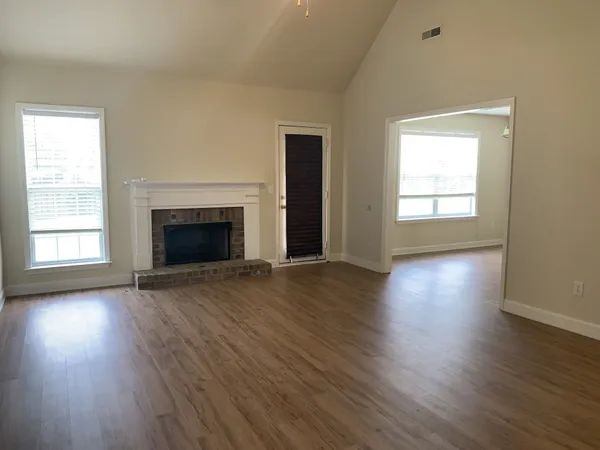 an empty room with wooden floor fireplace and windows
