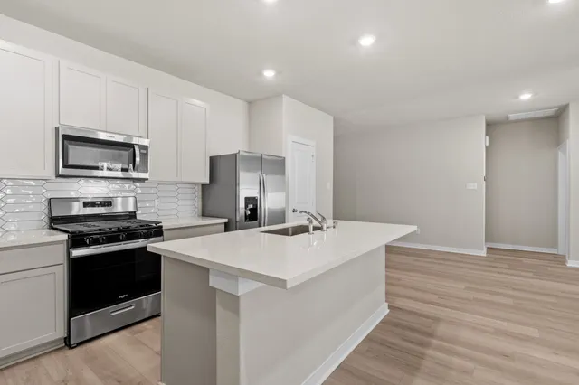 a kitchen with stainless steel appliances a stove top oven a sink dishwasher and a refrigerator with wooden floor