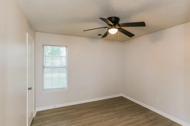 an empty room with wooden floor a ceiling fan and windows