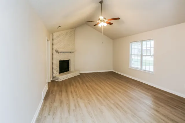 an empty room with wooden floor fireplace and windows