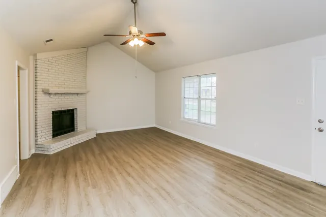 an empty room with wooden floor fireplace and windows