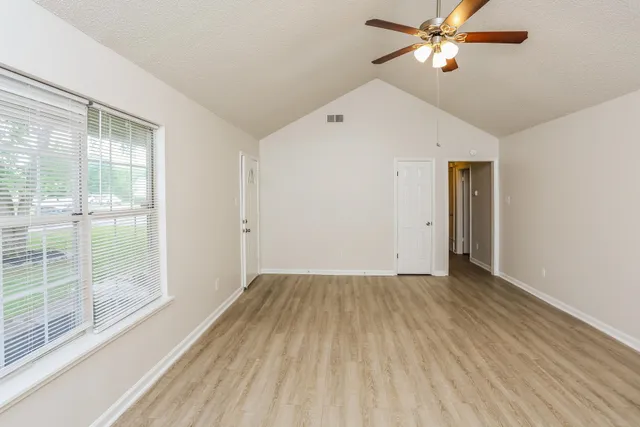 an empty room with wooden floor fan and windows