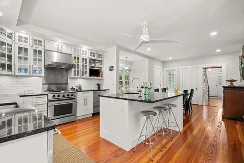 a kitchen with stainless steel appliances granite countertop a stove top oven a sink dishwasher a dining table and chairs with wooden floor