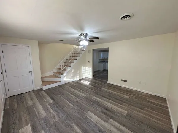a view of an empty room with wooden floor and a ceiling fan