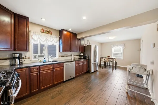 a large kitchen with stainless steel appliances granite countertop a stove top oven a sink a dining table and chairs with wooden floor