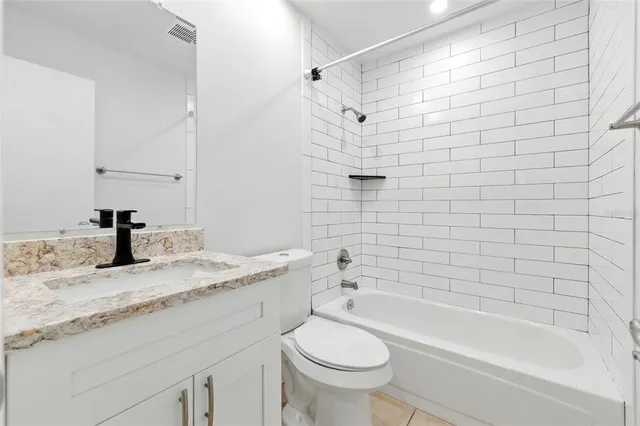 a bathroom with a granite countertop bathtub shower sink vanity and toilet