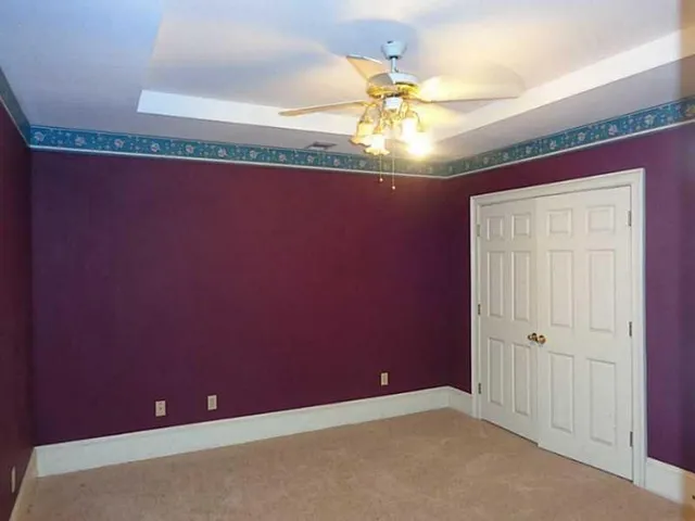 an empty room with a chandelier fan and wooden floor