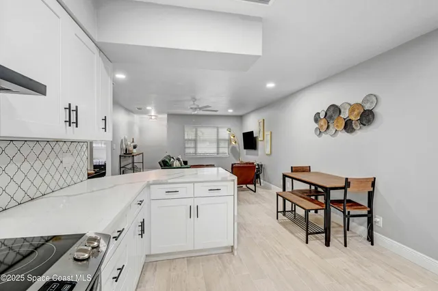 a large white kitchen with a stove a sink dishwasher and a dining table with wooden floor