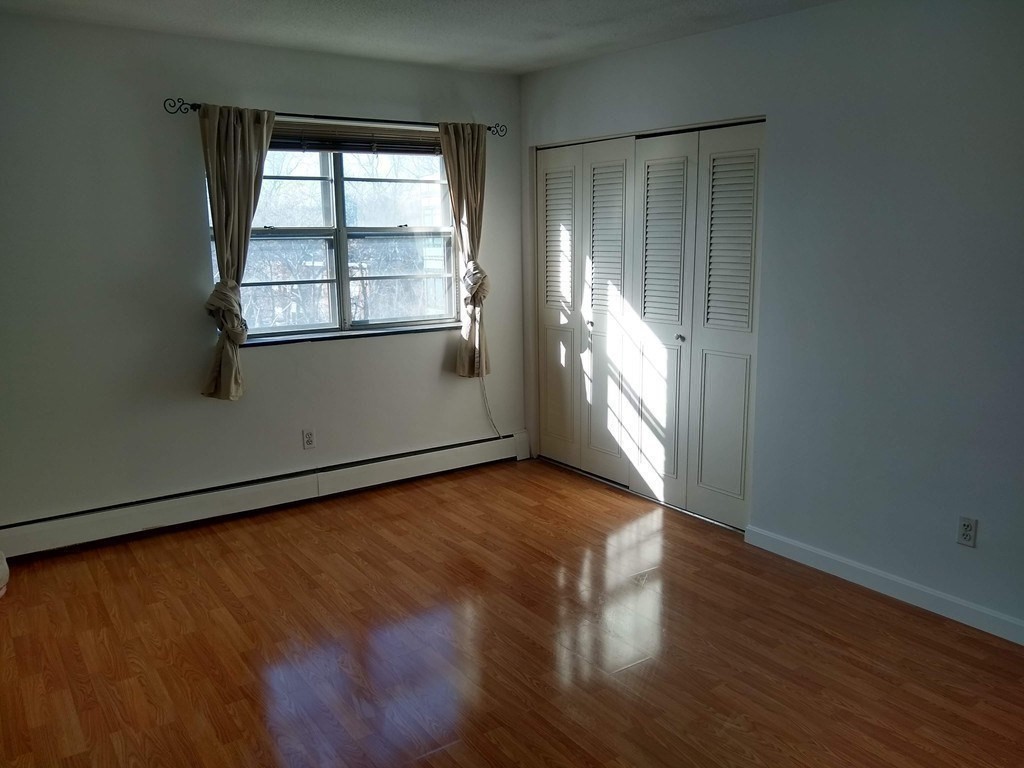 4925 Washington Street, Unit 406 Boston, MA 02132 - Photo 6 of 11 an empty room with wooden floor and windows
