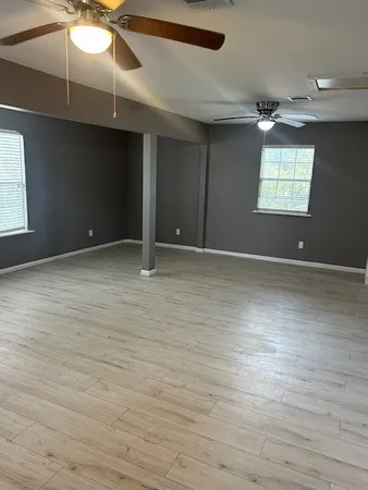 an empty room with wooden floor ceiling fan and windows
