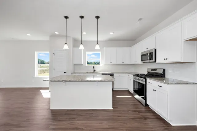 a large kitchen with stainless steel appliances kitchen island granite countertop a sink a stove a refrigerator and white cabinets