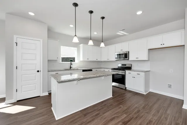 a kitchen with stainless steel appliances granite countertop a sink a stove a refrigerator and island with wooden floor