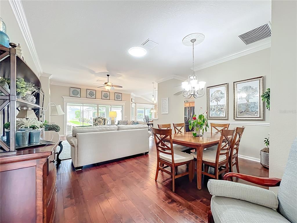 2875 Rain Lily Loop The Villages, FL 32163 - Photo 5 of 36 a dining room with wooden floor a chandelier a wooden table and chairs
