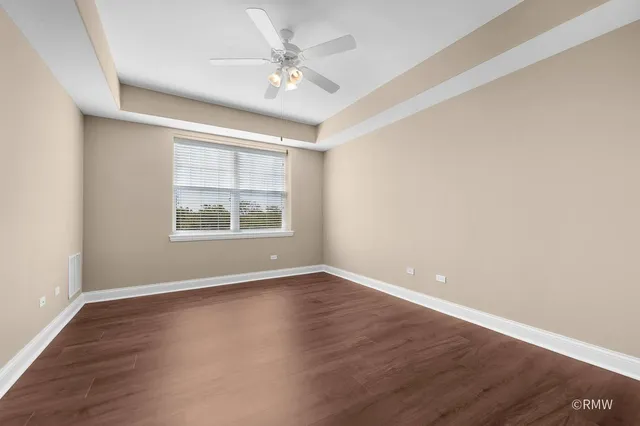 an empty room with wooden floor chandelier fan and windows