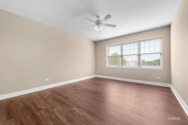 an empty room with wooden floor windows and fan