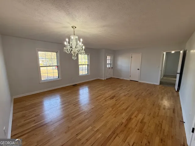 a view of an empty room with chandelier and wooden floor