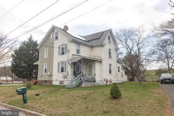 a view of a white house next to a yard with big trees