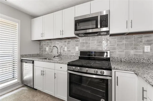 a kitchen with granite countertop white cabinets stove top oven and microwave