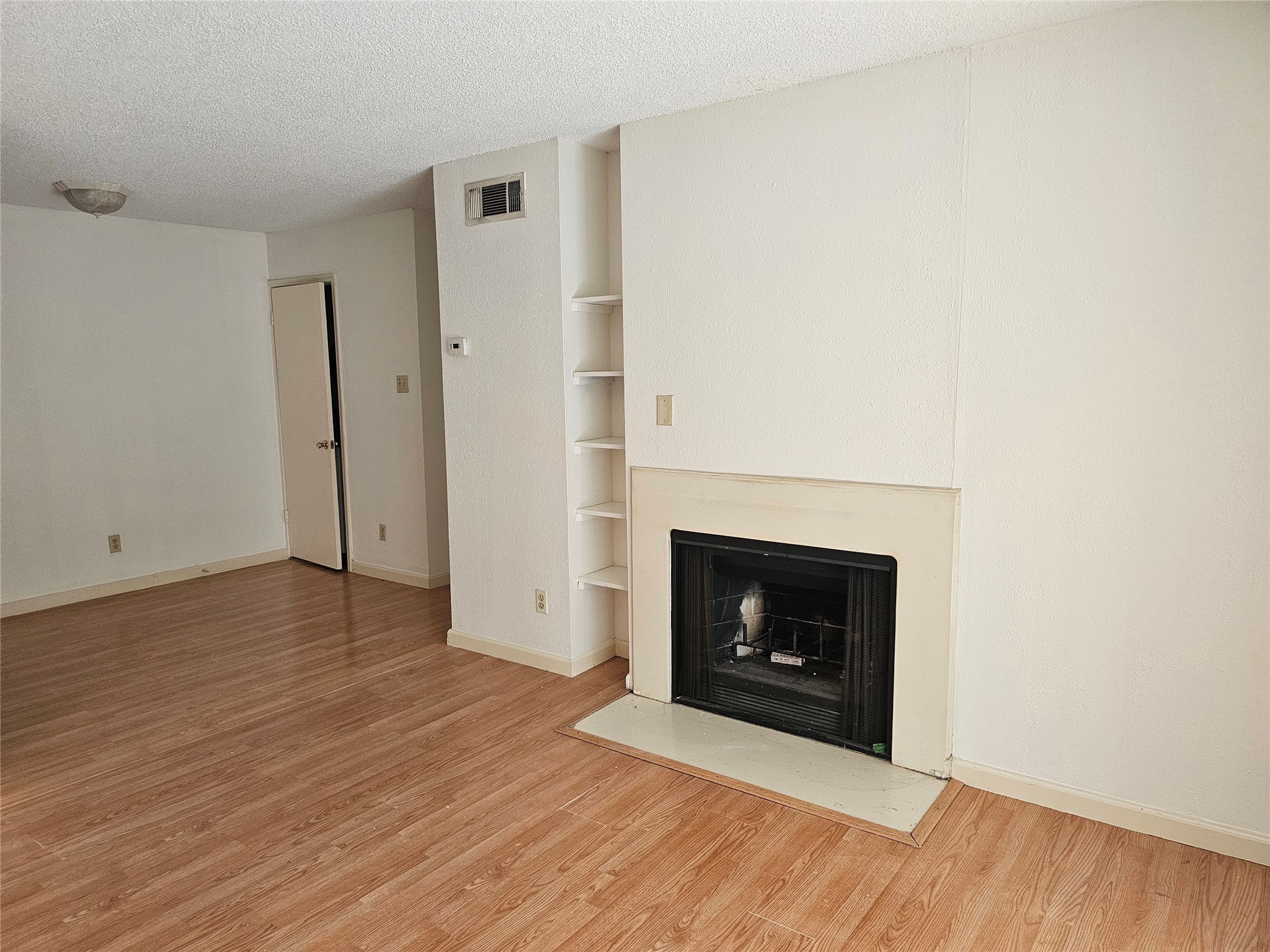 a view of an empty room with wooden floor and fireplace