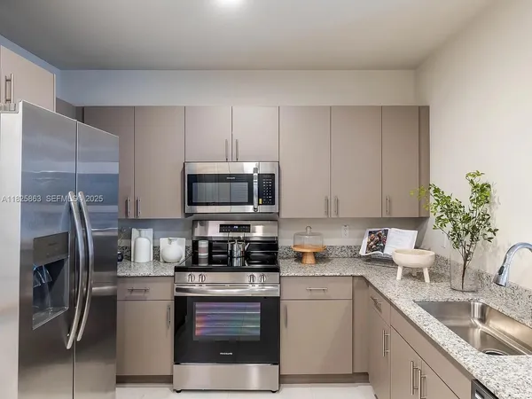 a kitchen with stainless steel appliances granite countertop a sink a stove a refrigerator and a white cabinets